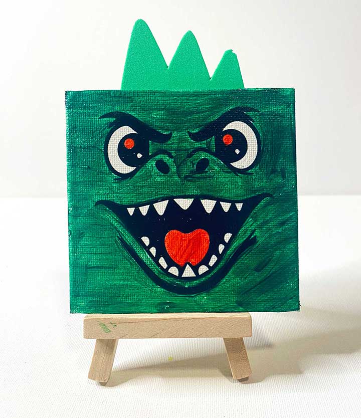 Finished kids painting of a green dinosaur / godzilla with a red eyes and green craft foam for a 3d effect on a white background